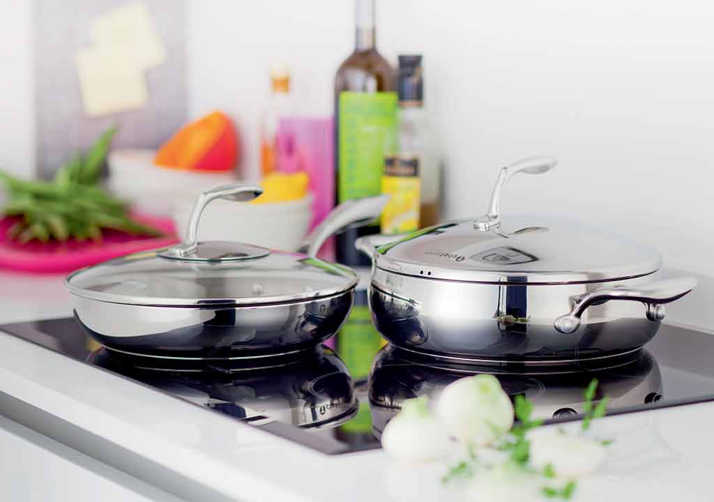 deux casseroles en acier inoxydable avec couvercles transparents posées sur une plaque de cuisson, entourées d'ingrédients et d'ustensiles de cuisine dans une cuisine lumineuse