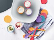 un ensemble de Set Pot À Yaourt Tupperware colorés avec couvercles assortis et cuillères, sur un torchon gris, près d’un bol de yaourt garni