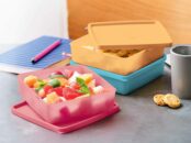 contenants alimentaires Cubix roses et bleus remplis de fruits frais et de biscuits sur un plan de travail avec un cahier et un crayon en arrière-plan